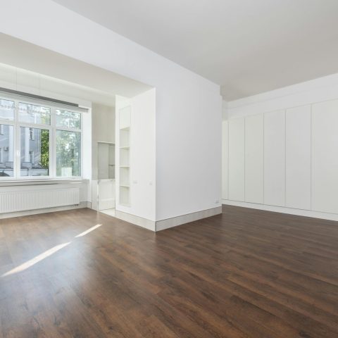 Bright empty room featuring large windows and wooden flooring.